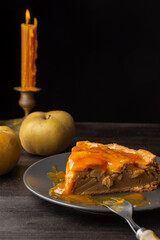 Closeup of a piece of apple pie with apricot jam with fork, on wooden table with apples and candle, in vertical