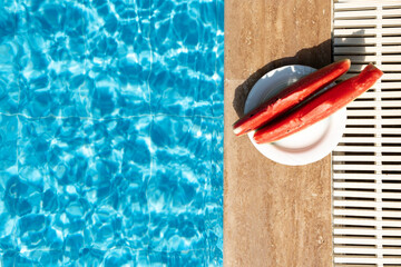 Fresh watermelon on border of swimming pool. Hot summer travel, vacation and holiday concept. Top view. Copy space