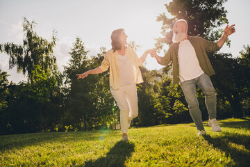 Full length photo of mature couple hold hands romantic forest go run green grass nature spring outdoors