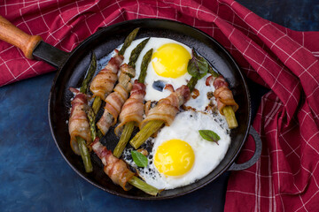 A dish of asparagus, bacon and eggs in a cast-iron skillet on a dark background.