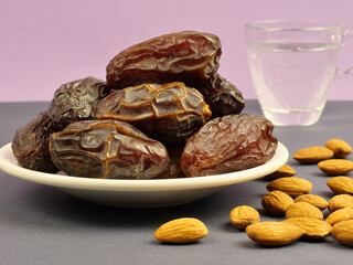 Dates. Dried dates on a plate, almonds and a glass of water on the table on a lilac background. Ramadan. Close-up.
