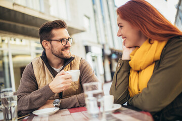Attractive young couple in love sitting at the cafe table outdoors, drinking coffee