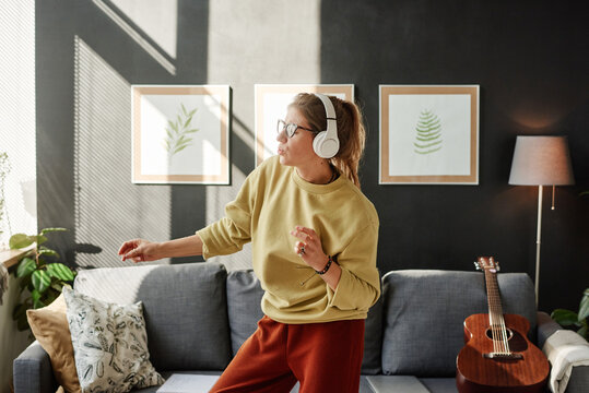 Young woman in wireless headphones enjoying the music and dancing in the living room at home