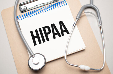 White notepad with the words hipaa and a stethoscope on a blue background. Medical concept