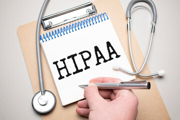 White notepad with the words hipaa and a stethoscope on a blue background. Medical concept
