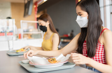 Obraz na płótnie Canvas Asian woman sitting separated in restaurant eating food .keep social distance for protect infection from coronavirus covid-19, restaurant and social distancing concept.