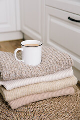 
A cup of hot coffee with milk on a stack of knitted clothes. Autumn mood. The concept of home comfort, cozy mood and winter morning. Hygge. Vertical photo.