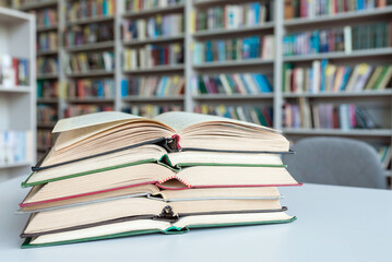 A stack of open books on the table in the library room. Library with bookcases. Large selection of books.