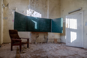 Fototapeta na wymiar A blackboard in an abandoned school. An old abandoned school. Shabby walls. Armchair in the room. An old abandoned building. Light rays pass through the window.