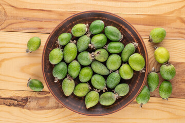 Several fragrant sweet feijoa fruits in earthenware, close-up, on a wooden table, top view.