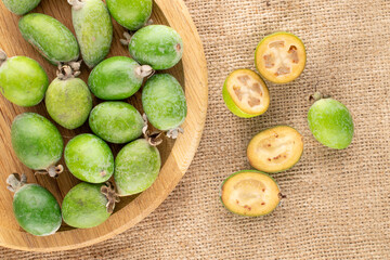 Several fragrant sweet feijoa fruits with a wooden tray on burlap, close-up, top view.