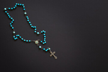 Rosary with blue beads on a black background with copy space