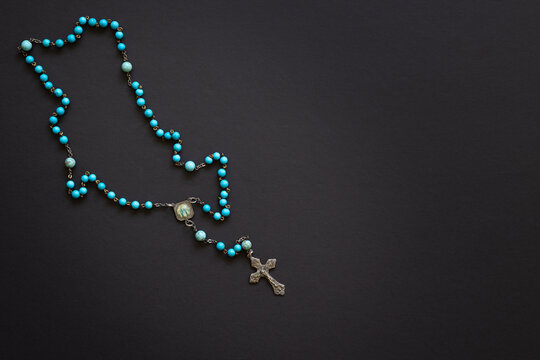 Rosary with blue beads on a black background with copy space