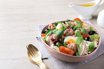 Bowl of delicious salad with canned tuna and vegetables served on white wooden table, space for text