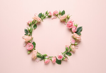 Wreath made of beautiful flowers and green leaves on pale pink background, flat lay. Space for text