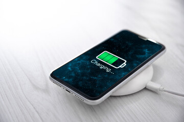 Mobile smart phone on wireless charging device on white background. Icon battery and charging progress lighting on screen.smartphones connected to power source.low battery level problems.Plugged Phone