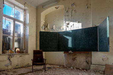 A blackboard in an abandoned school. An old abandoned school. Shabby walls. Armchair in the room. An old abandoned building. Light rays pass through the window.