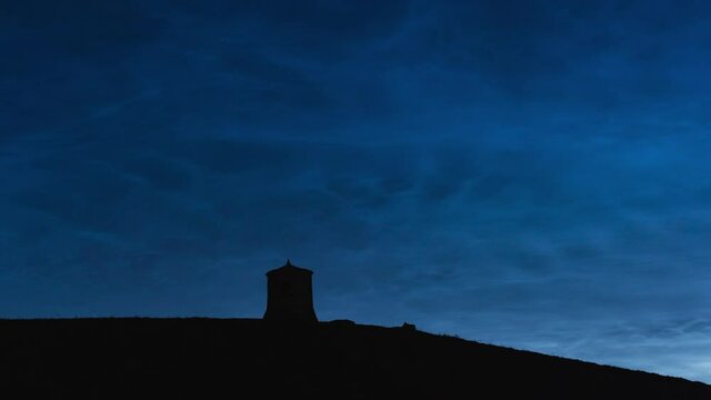 Noctilucent silver clouds in the night sky above the ancient tower on the hill timelapse 4K