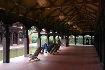 Fototapeta premium place of calmness and meditation: сourtyard of the tibetan temple with water pool, resting sitting people, wooden chairs in the Nepal Himalaya Park Stiftung in Bavaria, Germany.
