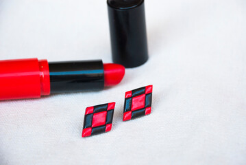 Fashion background with stud earrings and lipstick in red and black.