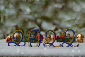 The number 2022 of blue and gold tinsel stands against the background of spruce branches and red and gold Christmas balls, the background is decorated with silver bokeh. New Year,Christmas banner, fly