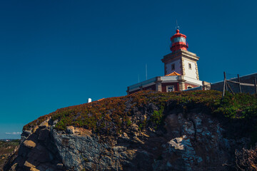 Fototapeta na wymiar Red and white lighthouse on a cliff on a sunny day