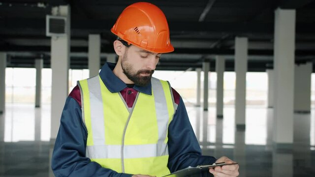 Construction inspector wearing uniform is checking papers and studying industrial building inside. Supervision and hse inspection concept.