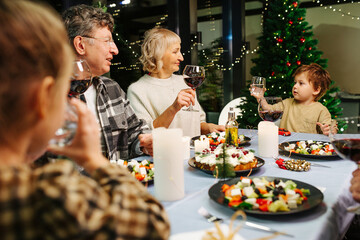 Big family on christmas gathering. Little boy wants to clink his water glass