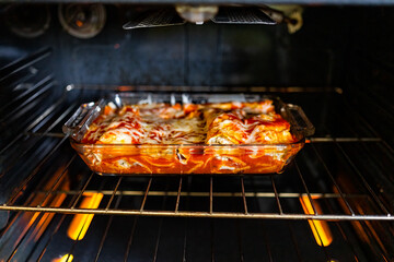 Inside oven with rack and homemade Mexican food enchiladas in baking tray glass dish cooking with...