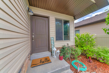 Facade of house with beige vinyl lap siding and gray front door near the window