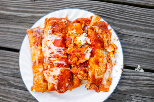 Flat top above view of plate with pile of homemade Mexican food enchiladas with tomato sauce, tortilla and melted cheese