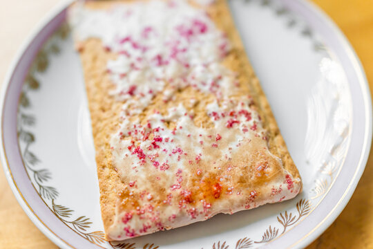 One pink toaster pastry with frosting, sprinkles, and red pink cherry or strawberry sweet filling on plate macro closeup