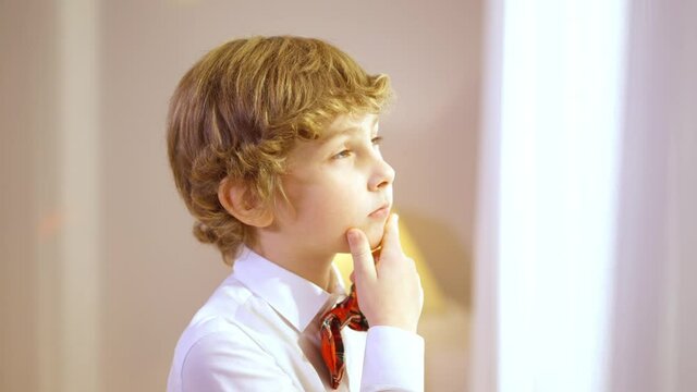 Little adorable boy looking out the window waiting for Santa Clause on Christmas eve at home. Portrait of cute charming Caucasian kid in shirt and bow tie indoors on New Year. Childhood concept