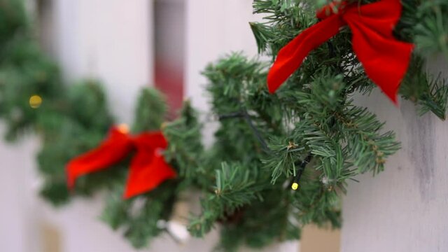 Christmas green garland with lights and red bows on white fence. Holiday concept.