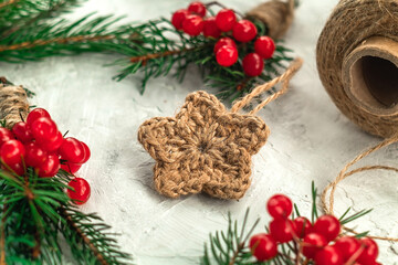 Christmas composition with a snowflake knitted with jute among spruce branches with red berries on a light background. Christmas concept.
