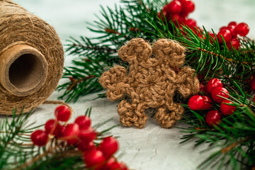 Christmas decor. A snowflake knitted with jute among the branches of the Christmas tree and red berries.