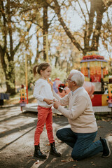 Fototapeta premium Grandfather having fun with his little granddaughter in the amusement park
