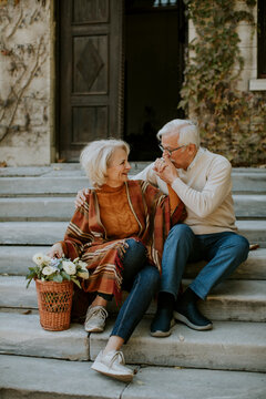 Senior Couple Sitting On Stairs With Basket Full Of Flowers And Groceries