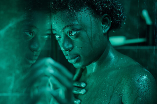 African wet woman looking through the glass wall while standing in the shower cabine