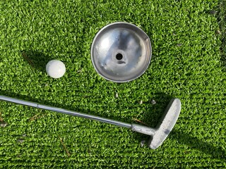 Mini golf putter and ball near the hole on artificial grass playing track. Miniature golf course.