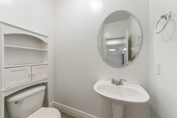 White powder room interior with toilet and sink with oval mirror