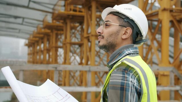 Portrait of engineer planning work at construction site looking at blueprint outdoors in industrial zone. People and occupation concept.