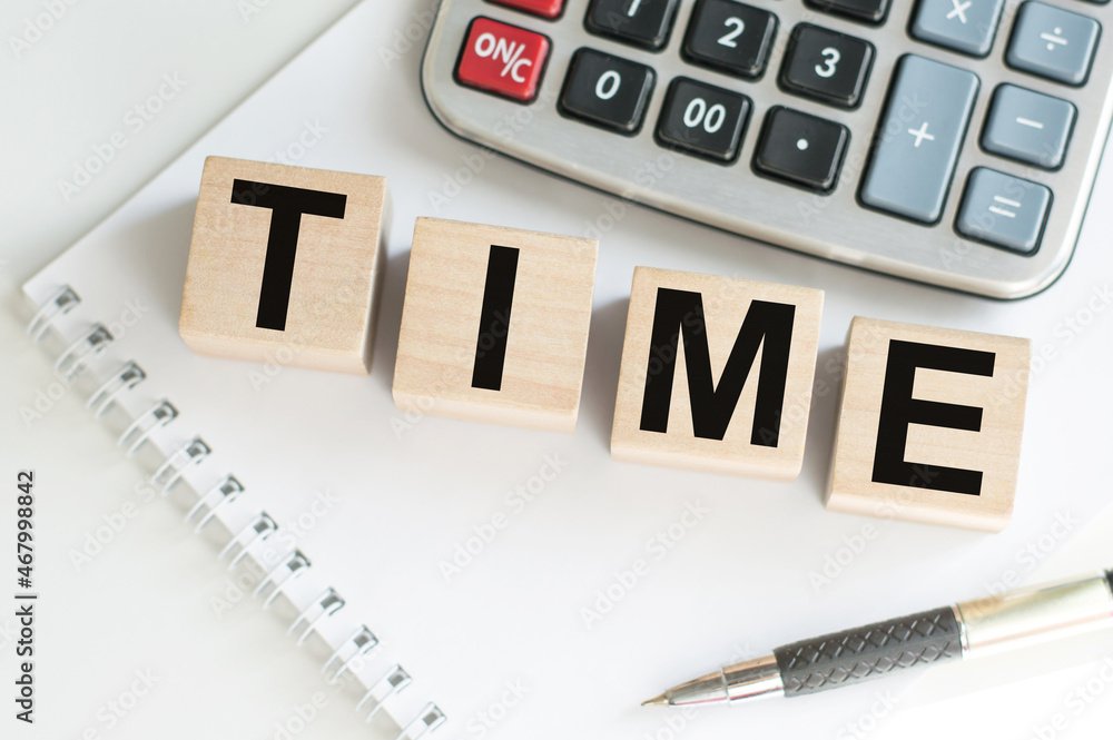 Poster text time on wooden cubes on a notebook next to a pen and a calculator on the table.