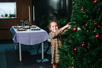 Cheeky proud little girl decorating a christmas tree with red shiny balls