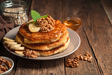 A stack of homemade pancakes with honey and nuts and a banana on a wooden background.
