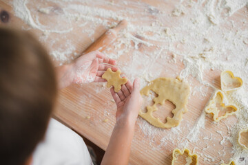 Home cooking concept: close-up of children's hands who cut a blank cookie from raw dough in the form of a bear.
