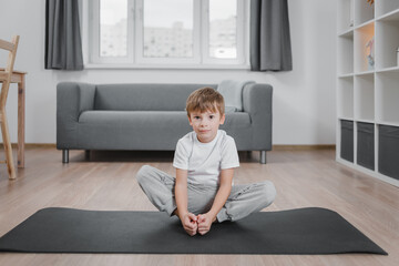 Boy child doing butterfly exercise for mobility of the hip joints on floor on a sports mat in home...