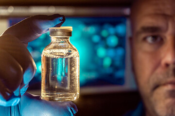 Close-up of an injectable vial with medicine, with the background out of focus of a male scientist.