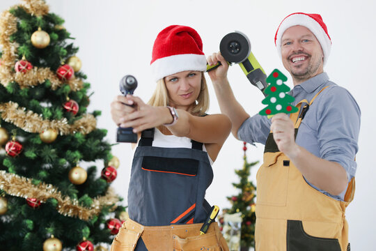 Young smiling builders woman and man in santa claus hats with tools on the background of New Year tree.