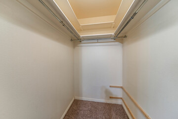 Empty narrow walk-in closet with top shelves and metal rods